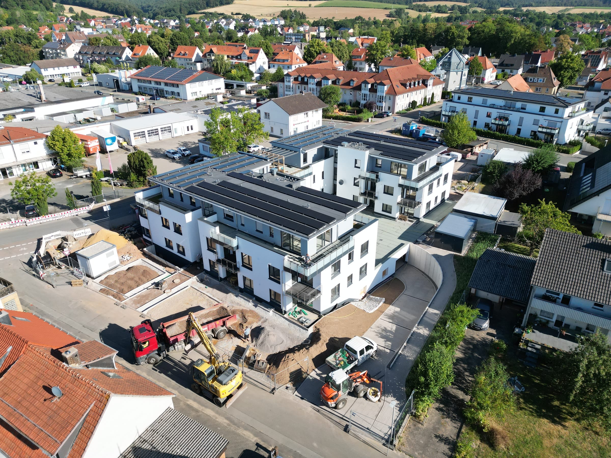 Luftaufnahme des Wohnprojekts in Bad Arolsen: zwei fertiggestellte Gebäudeteile mit Photovoltaik auf den Dächern, davor die Außenanlagen im Bau